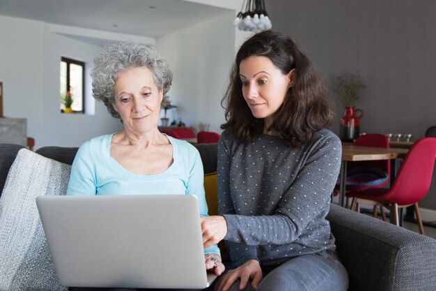 Giovane donna spiegando la nonna come utilizzare il computer portatile