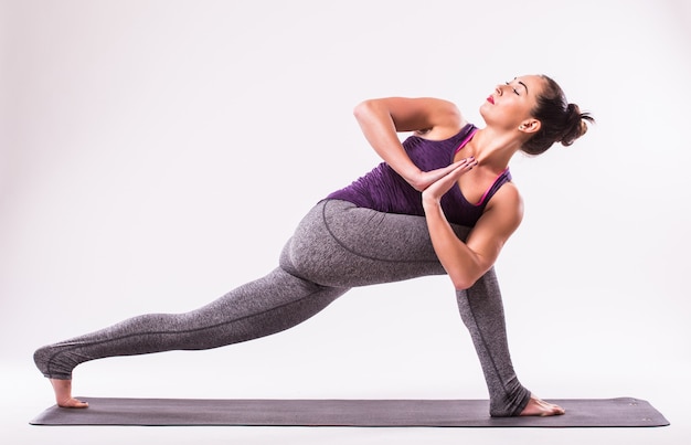 Giovane donna sportiva che fa pratica yoga isolata su priorità bassa bianca - il concetto di vita sana e l'equilibrio naturale tra il corpo e lo sviluppo mentale