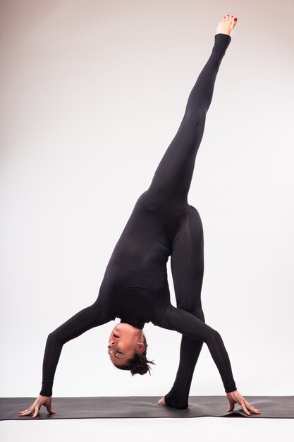 Giovane donna sportiva che fa pratica yoga isolata su priorità bassa bianca - il concetto di vita sana e l'equilibrio naturale tra il corpo e lo sviluppo mentale