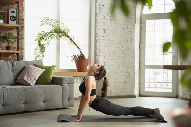 Giovane donna sportiva che prende le lezioni di yoga online e le pratiche a casa