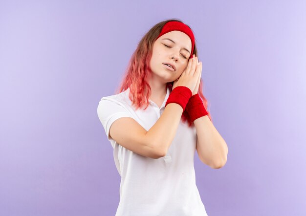 Giovane donna sportiva che tiene insieme le palme che si appoggia la testa sui palmi che sembrano stanchi vuole dormire in piedi sopra la parete viola