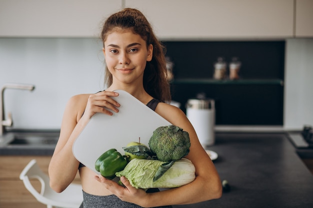 Giovane donna sportiva con bilance e verdure in cucina