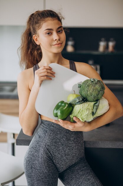 Giovane donna sportiva con bilance e verdure in cucina