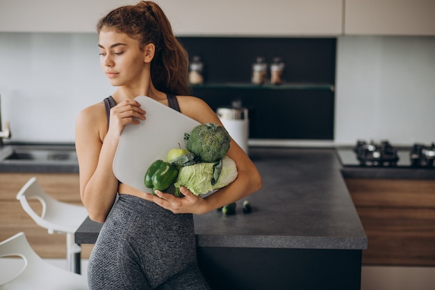 Giovane donna sportiva con bilance e verdure in cucina