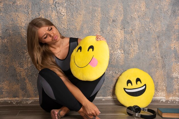 Giovane donna sportiva in abiti sportivi in possesso di un sorridente e con la lingua fuori i cuscini emoji