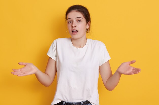 Giovane donna stupita del brunette che spande le palme da parte, scrollando le spalle le spalle