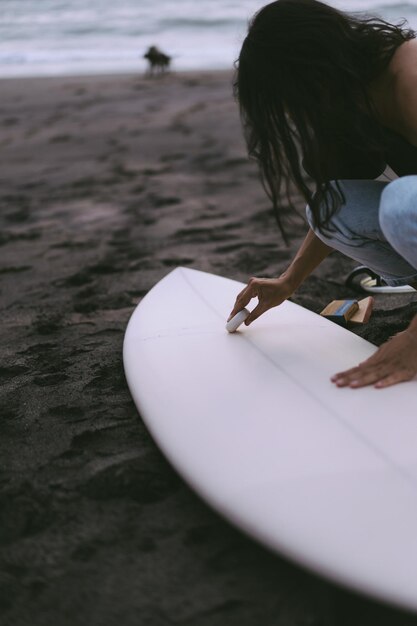 Giovane donna surfista preparare una tavola da surf sull'oceano ceretta Donna con tavola da surf sull'oceano sport acquatici stile di vita attivo