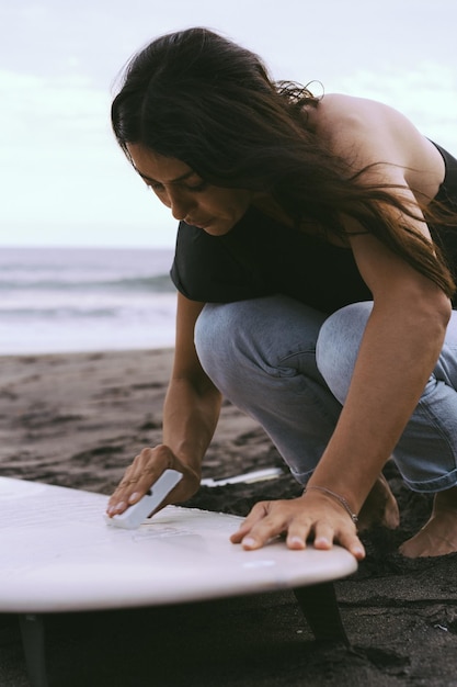 Giovane donna surfista preparare una tavola da surf sull'oceano ceretta Donna con tavola da surf sull'oceano sport acquatici stile di vita attivo