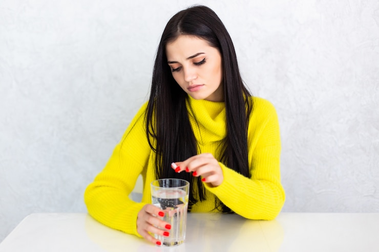 Foto gratuito giovane donna sveglia del brunette che cattura una pillola con un bicchiere d'acqua a casa