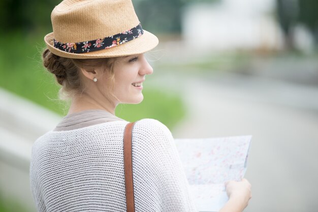 Giovane donna viaggiatrice in cappello di paglia azienda mappa. Vista laterale posteriore