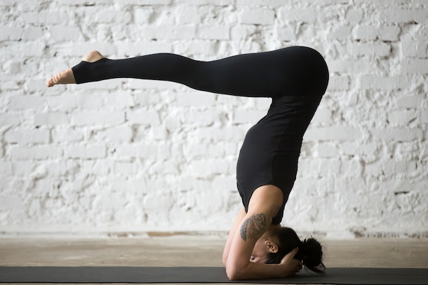 Giovane donna yogi attraente in posa headstand, backgr loft bianco