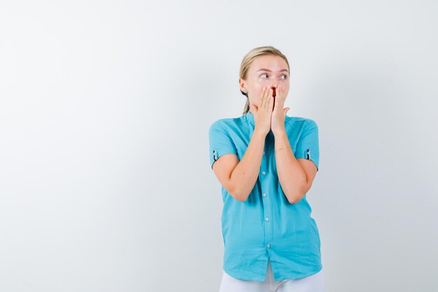 Giovane dottoressa che si tiene per mano sulla bocca in uniforme medica, maschera e sembra perplessa