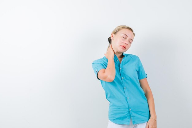 Giovane dottoressa che tiene la mano sul collo in uniforme medica, maschera e sembra esausta