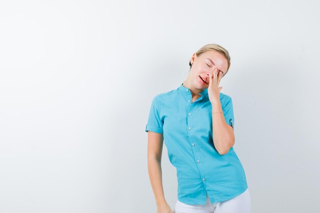 Giovane dottoressa che tiene la mano sull'occhio in uniforme medica, maschera e sembra assonnata