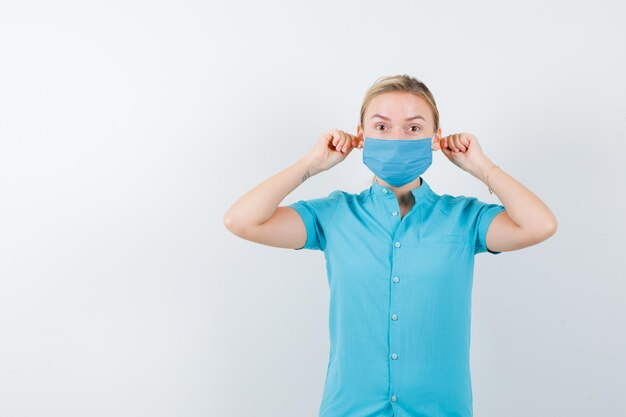 Giovane dottoressa che tira i lobi delle orecchie con le dita in uniforme isolata