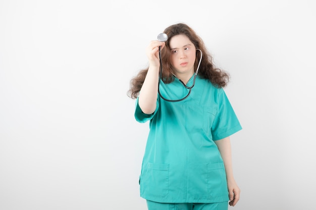 Giovane dottoressa con sindrome di down utilizzando uno stetoscopio sul muro bianco.