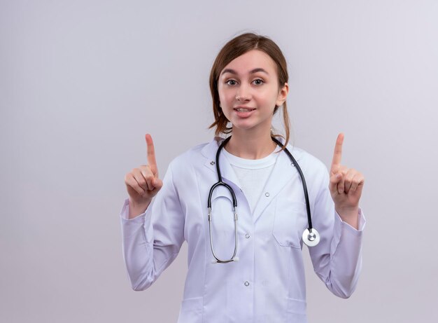 Giovane dottoressa impressionata che indossa veste medica e stetoscopio con le dita sollevate con spazio di copia