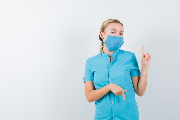 Giovane dottoressa in uniforme che punta su e giù e sembra sicura isolata