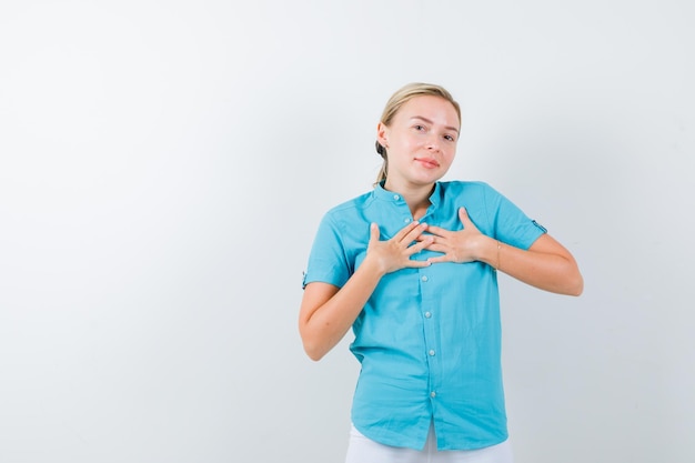 Giovane dottoressa in uniforme medica, maschera che si tiene per mano sul petto e sembra speranzosa