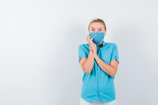 Giovane dottoressa in uniforme medica, maschera che tiene la mano sulla guancia e sembra spaventata