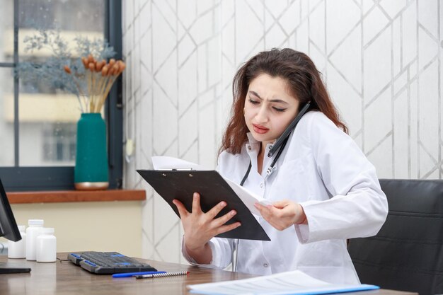 Giovane dottoressa parlando al telefono e guardando il suo taccuino