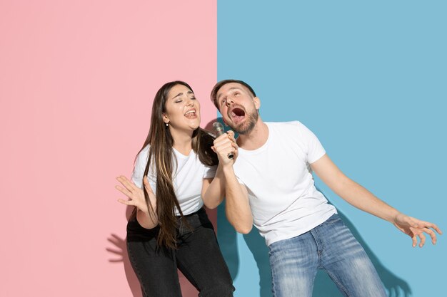 Giovane e felice uomo e donna in abiti casual sulla parete bicolore rosa, blu, cantando