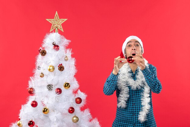 Giovane emozionante divertente emotivo sorridente con il cappello di Babbo Natale in una camicia spogliata blu