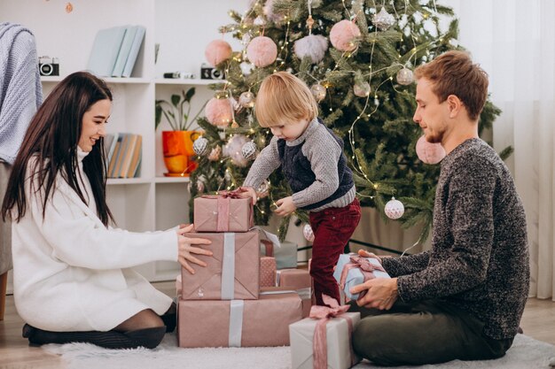 Giovane famiglia che disimballa i regali con il piccolo figlio dall'albero di Natale