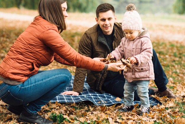 Giovane famiglia che gioca con le foglie nella foresta di autunno