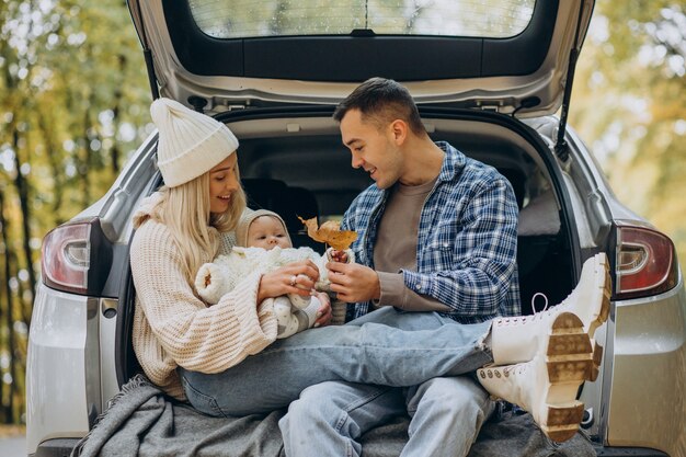 Giovane famiglia con la nostra bambina seduta nel retro della loro auto nella foresta autunnale