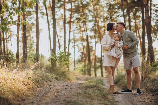 Giovane famiglia con la piccola figlia sveglia che cammina nella foresta sul tramonto