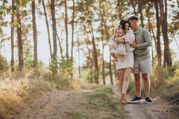 Giovane famiglia con la piccola figlia sveglia che cammina nella foresta sul tramonto