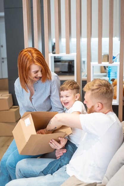 Giovane famiglia felice con il bambino che disimballa le scatole che si siedono insieme sul sofà