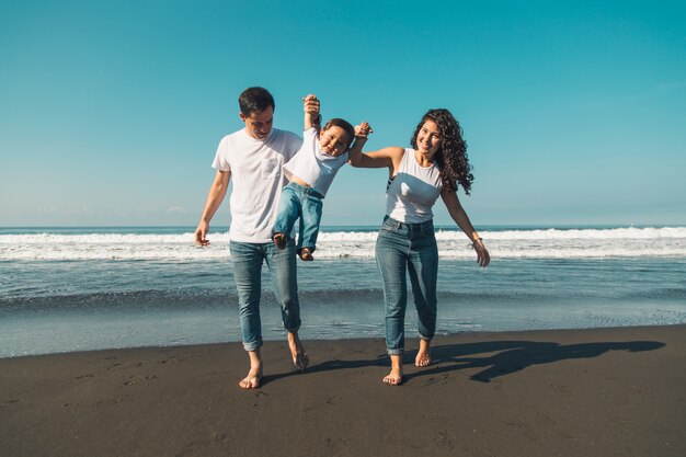 Giovane famiglia felice divertendosi con il bambino sulla spiaggia soleggiata