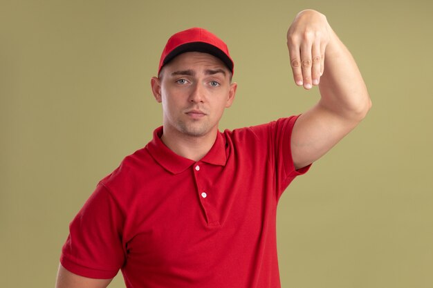 Giovane fattorino che indossa l'uniforme e cappuccio che finge di tenere qualcosa di isolato sulla parete verde oliva