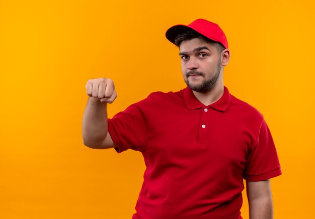 Giovane fattorino in uniforme rossa e cappuccio che mostra il pugno che guarda l'obbiettivo con la faccia seria