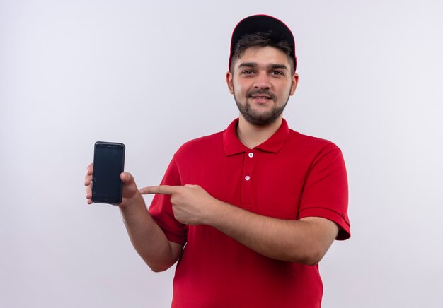 Giovane fattorino in uniforme rossa e cappuccio che mostra smartphone che punta con il dito sorridendo fiducioso