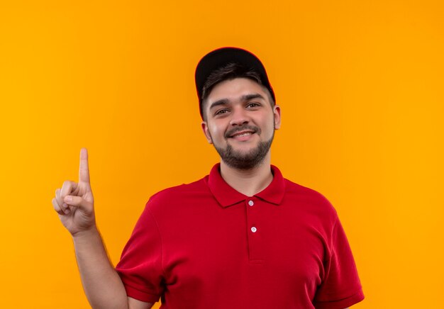 Giovane fattorino in uniforme rossa e cappuccio sorridente che mostra il dito indice