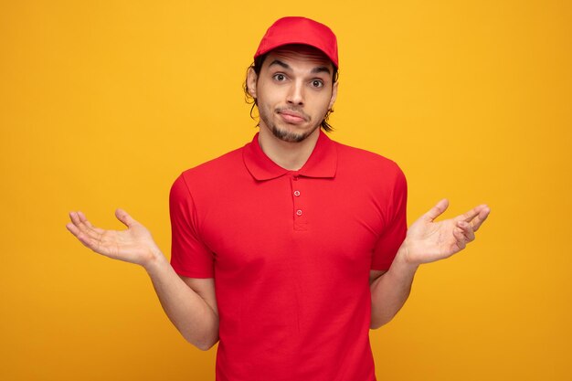 giovane fattorino senza tracce che indossa l'uniforme e il cappuccio guardando la fotocamera che mostra le mani vuote isolate su sfondo giallo