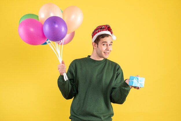 Giovane felice di vista frontale con il cappello della Santa e palloncini colorati in piedi sul giallo