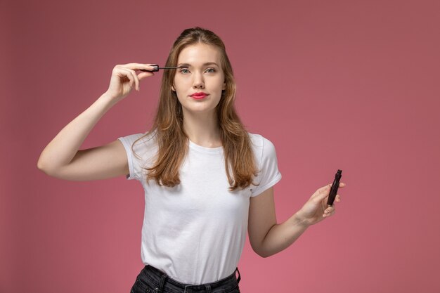 Giovane femmina attraente di vista frontale che sorride e che fa il suo trucco sulla ragazza della femmina di colore del modello della parete rosa scuro