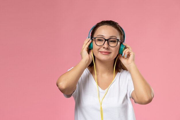 Giovane femmina attraente di vista frontale in maglietta bianca che posa appena e che ascolta la musica tramite gli auricolari sui precedenti rosa