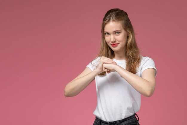 Giovane femmina attraente di vista frontale in maglietta bianca che sorride e che stringe i pugni sulla ragazza femminile di colore rosa del modello della scrivania