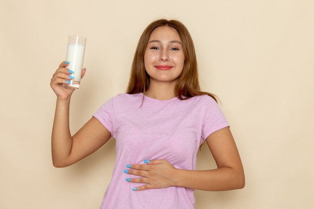 Giovane femmina attraente di vista frontale in maglietta rosa e blue jeans che beve latte con il sorriso