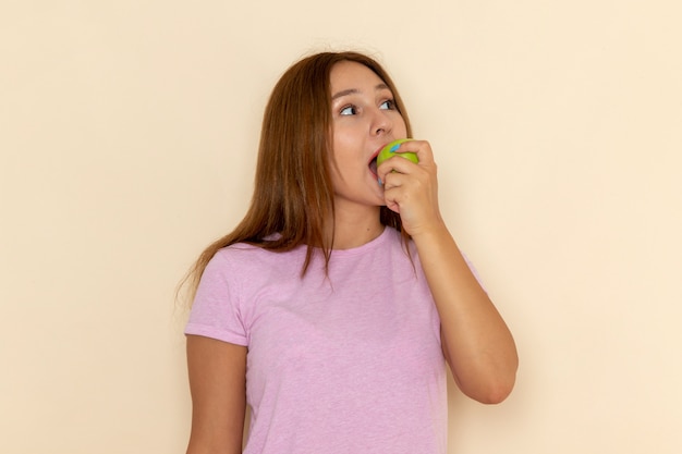 Giovane femmina attraente di vista frontale in maglietta rosa e blue jeans che mordono la mela verde