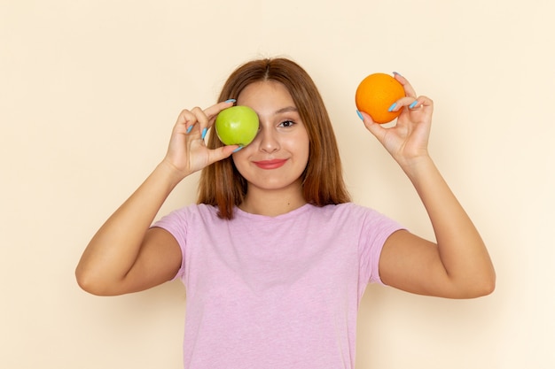 Giovane femmina attraente di vista frontale in maglietta rosa e blue jeans che tengono mela arancione e posa
