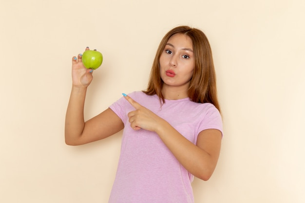 Giovane femmina attraente di vista frontale in maglietta rosa e blue jeans che tengono mela e che la indica