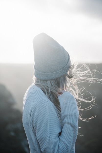 Giovane femmina bionda con un cappello che cammina sulla spiaggia in un tempo ventoso