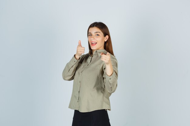 Giovane femmina che indica alla macchina fotografica in camicia, gonna e che sembra felice