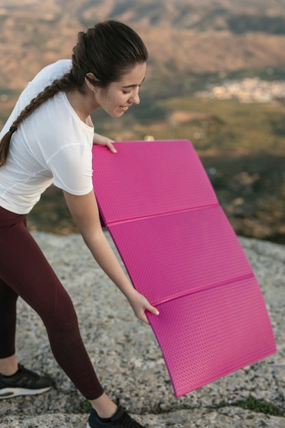 Giovane femmina che mette la stuoia di yoga sulla montagna